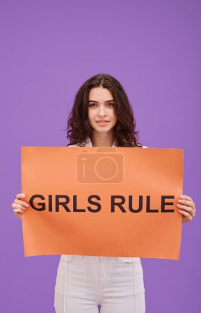 Photo for Portrait of young woman holding Girls Rule placard and looking at camera on purple background, she expressing her opinion - Royalty Free Image