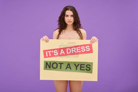 Photo for Portrait of young shirtless woman holding Its a dress not a yes poster in front of her standing against color background - Royalty Free Image