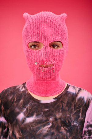 Photo for Portrait of young woman in pink balaclava with pinned closed mouth looking at camera on pink background - Royalty Free Image