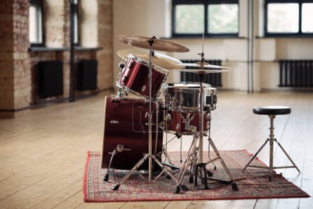 Horizontal image of drum kit for drummer standing on carpet at big empty studio