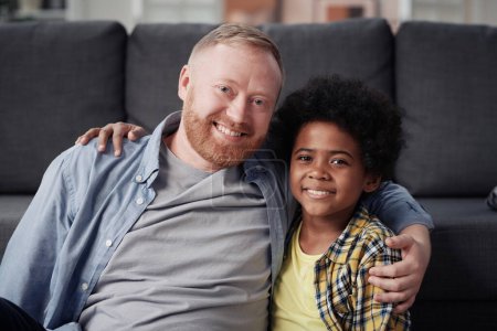Foto de Retrato de papá e hijo adoptivo abrazando y sonriendo a la cámara sentada en casa - Imagen libre de derechos