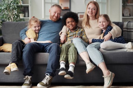 Retrato de una gran familia adoptiva con niños sentados en el sofá, abrazándose y sonriendo a la cámara