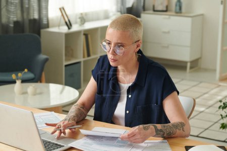 Mujer seria económica en gafas que trabajan en el ordenador portátil en casa para pagar las facturas y los impuestos sobre el gadget en línea