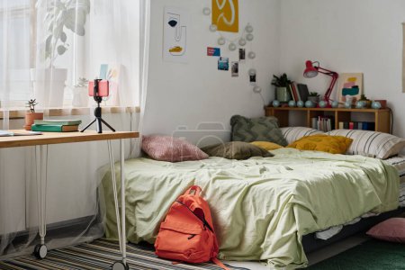 Horizontal image of teenage room with cozy bed and table with smartphone on tripod