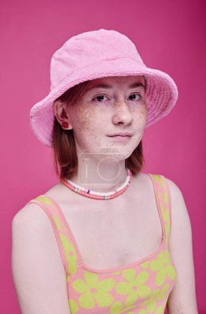 Photo for Portrait of teenage girl with freckles in pink panama hat looking at camera against pink background - Royalty Free Image