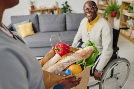 Primer plano del cuidador sosteniendo una bolsa de papel con comida que lleva a casa para el hombre con discapacidad