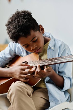 Africain garçon examiner les notes à la guitare alors qu'il apprend à jouer de l'instrument de musique à la leçon
