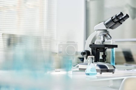 Foto de Microscopio de pie en el lugar de trabajo del científico o clínico moderno con grupo de frascos y otros artículos de vidrio con sustancias líquidas - Imagen libre de derechos