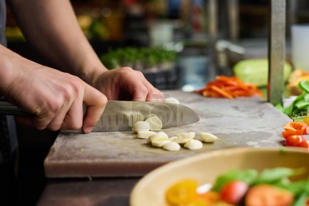 Hands of young male chef slicing pieces of fresh mozarella cheese on chopping board while preparing ingredients for salad in the kitchen-stock-photo