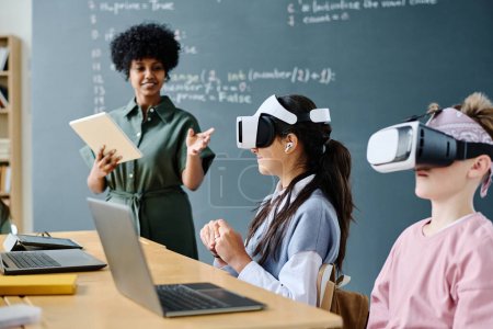 Photo for Students using VR glasses while sitting at table and listening to teacher at IT lesson - Royalty Free Image