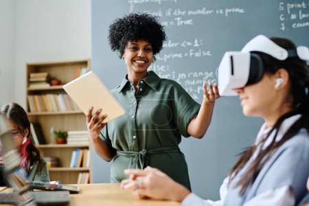 Photo for Smiling African American teacher having IT lesson with students while they using VR glasses - Royalty Free Image