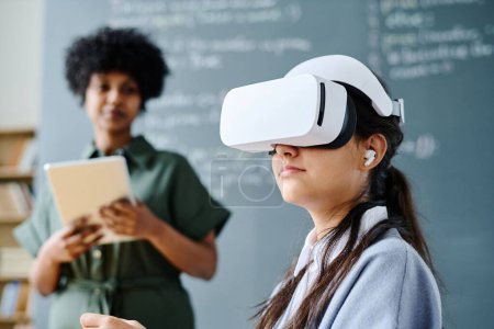 Photo for Student in VR glasses sitting at lesson with teacher explaining material in background - Royalty Free Image