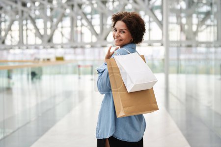 Photo for Joyful black girl posing with paper bags with purchases at mall looking at camera over shoulder - Royalty Free Image
