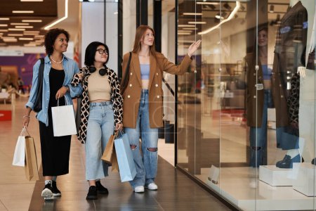 Photo for Full shot of multiracial group of young girls walking around shopping mall observing shop windows - Royalty Free Image
