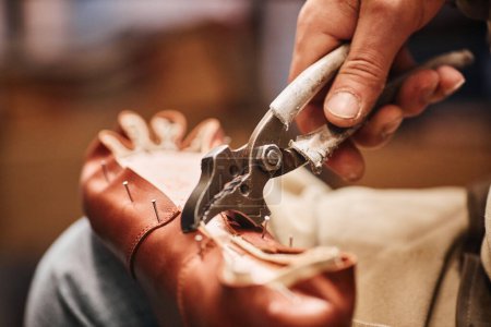 Photo for Metallic pliers in hand of male shoemaker fixing upper part of boot to sole while sitting in front of camera and working over client order - Royalty Free Image
