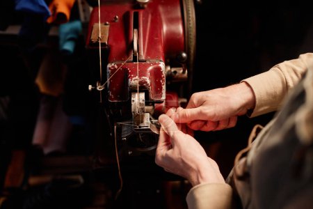 Téléchargez les photos : Vue ci-dessus du jeune artisan mâle dans le tablier de fixation des détails de la machine à coudre électrique tout en se tenant devant l'équipement dans l'atelier - en image libre de droit
