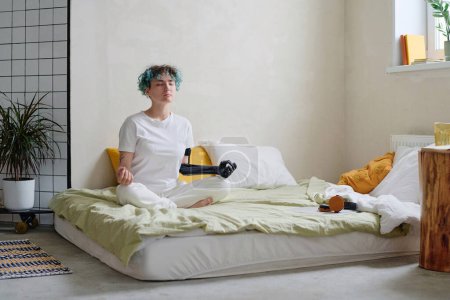 Foto de Adolescente con brazo protésico meditando en la cama por la mañana - Imagen libre de derechos