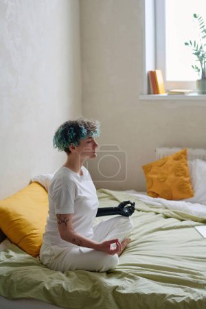 Foto de Mujer joven con cabello rizado verde meditando en la cama por la mañana - Imagen libre de derechos