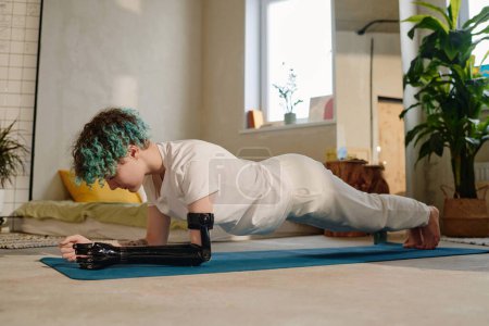 Photo for Amputee teenage girl doing plank position to on yoga mat when working out at home in morning - Royalty Free Image
