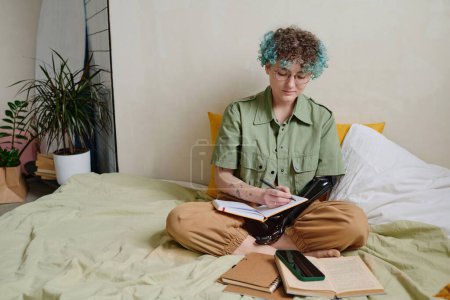 Photo for Student with prosthetic arm sitting on bed and writing down plans for day - Royalty Free Image