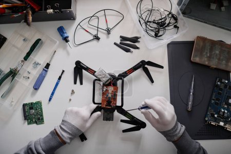 Photo for Flat lay shot of hands of unrecognizable repairman fixing broken quadcopter with screwdriver - Royalty Free Image