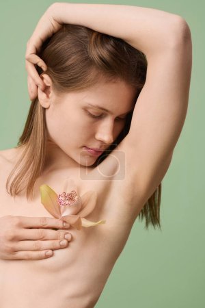 Photo for Medium close-up studio portrait of young Caucasian woman holding orchid flower posing topless, breast cancer awareness and body positivity concept - Royalty Free Image