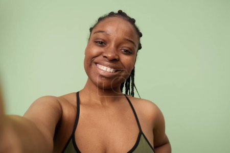 Foto de Medio primer plano POV de autoconfianza gen Z Chica negra sin maquillaje de pie en el estudio tomando selfie - Imagen libre de derechos