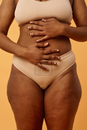 Photo for Conceptual studio shot of unrecognizable young Black woman in underwear posing for camera with hands on her belly - Royalty Free Image