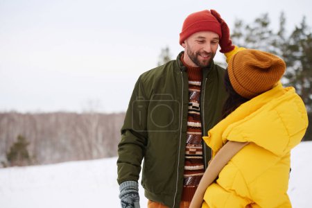 Unrecognizable young woman wearing puffer jacket standing outdoors on winter day patting head of her husband, copy space