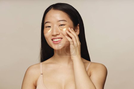 Medium closeup studio shot of young Asian woman posing for camera with collagen patches under eyes
