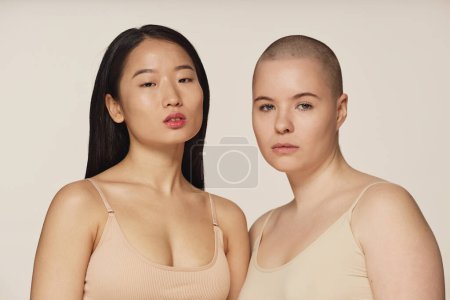 Medium closeup studio portrait of diverse young Asian and Caucasian women wearing neutral toned underwear posing for camera
