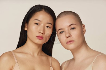 Medium closeup studio portrait of diverse young Asian and Caucasian girl friends wearing neutral toned underwear looking at camera