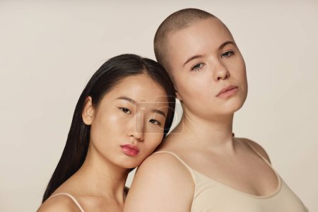 Medium closeup studio portrait of two diverse young Asian and Caucasian female friends wearing neutral toned bras posing for camera