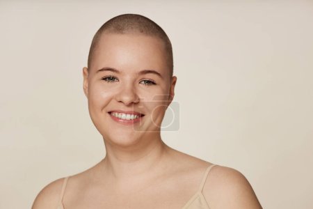 Medium closeup studio portrait of cheerful young Caucasian woman with shaved head smiling at camera