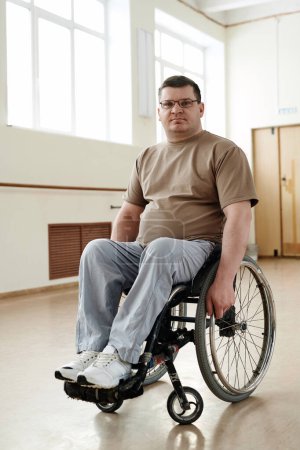 Vertical long shot of modern mature Caucasian with disability man in wheelchair in dance studio
