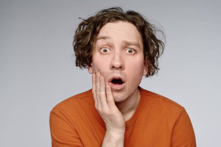 Medium closeup studio portrait of young Caucasian man with wavy hair looking at camera showing surprise emotion, copy space