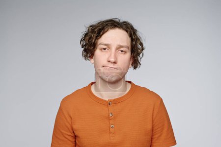 Brustbild eines jungen kaukasischen Mannes mit gelangweiltem Gesichtsausdruck, der in die Kamera blickt, grauer Hintergrund, Kopierraum