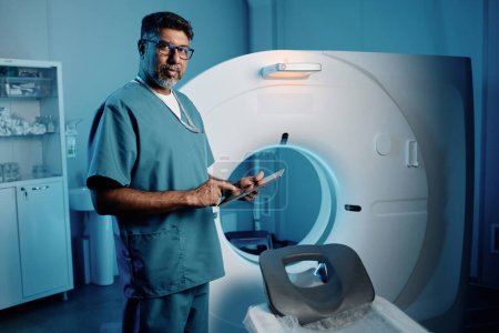 Plan moyen long du médecin biracial debout par IRM scanner tenant tablette numérique regardant la caméra, l'espace de copie