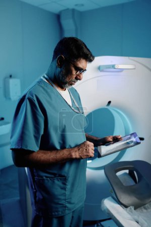 Plan vertical moyen d'un médecin biracial mature utilisant une tablette numérique au travail dans une salle d'IRM moderne, espace de copie