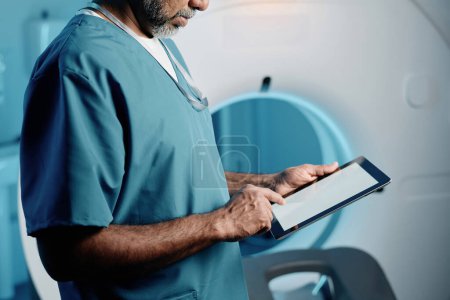 Prise de vue moyenne du médecin biracial en utilisant une tablette numérique au travail dans la salle d'IRM, espace de copie