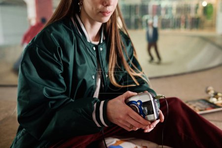 Crop shot of young woman in stylish streetwear listening to music with use of old portable player and headphones, copy space