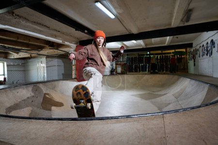 Long shot of self-confident young Caucasian woman practicing bowl ride on skateboard in skatepark, copy space