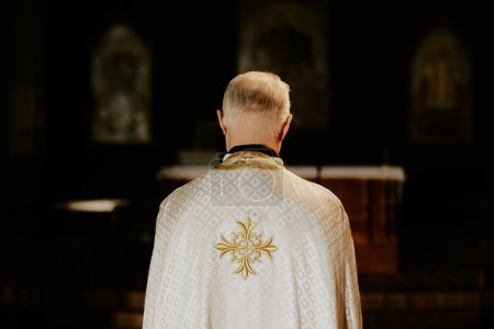 Back view of unrecognizable senior Catholic priest wearing chasuble standing indoors, copy space