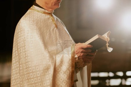 Crop shot of unrecognizable senior Catholic priest wearing liturgical vestment reading Bible, copy space