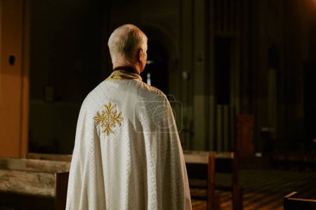 Vue arrière d'un prêtre catholique âgé méconnaissable portant un vêtement debout dans une église vide, espace de copie