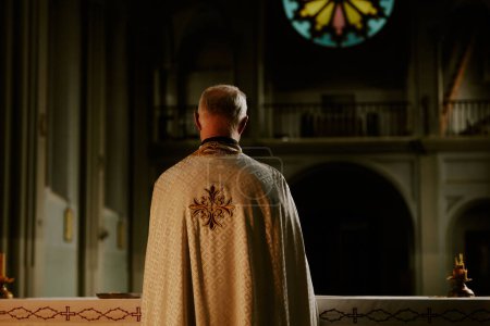 Rückansicht eines nicht wiederzuerkennenden katholischen Priesters, der am Tisch steht und sich auf den Abendmahlsritus in der Kirche vorbereitet