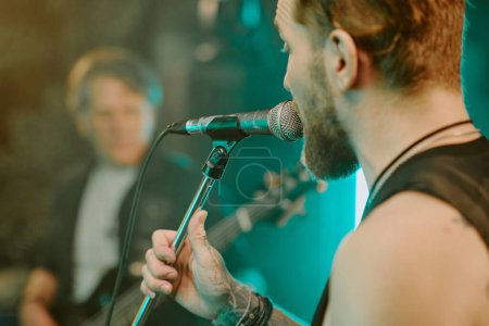 Closeup shot of young Caucasian male vocalist singing heavy metal song into microphone on stage