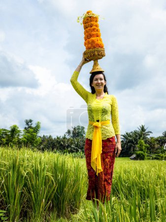 Téléchargez les photos : Femme blanche vêtue d'un costume balinais traditionnel portant les offrandes de Dieu pour la cérémonie religieuse hindoue. Culture et religion. Offrandes faites de fleurs de souci. Riz à Bali, Indonésie - en image libre de droit