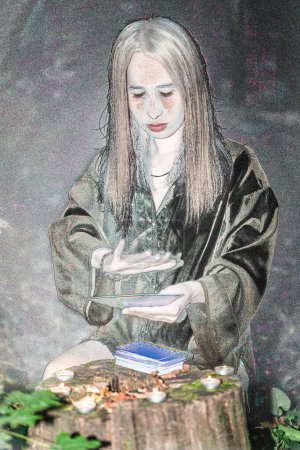 Téléchargez les photos : Une femme aux cheveux longs pose des cartes Tarot. Forêt diseur de bonne aventure, sorcière. - en image libre de droit