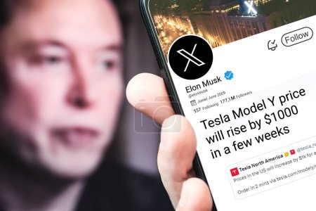 Photo for Poltava, Ukraine - March 16, 2024: Elon Musk Twitter profile page with a new tweet on a smartphone in his hand. In the background is a defocused portrait of Elon Musk. - Royalty Free Image